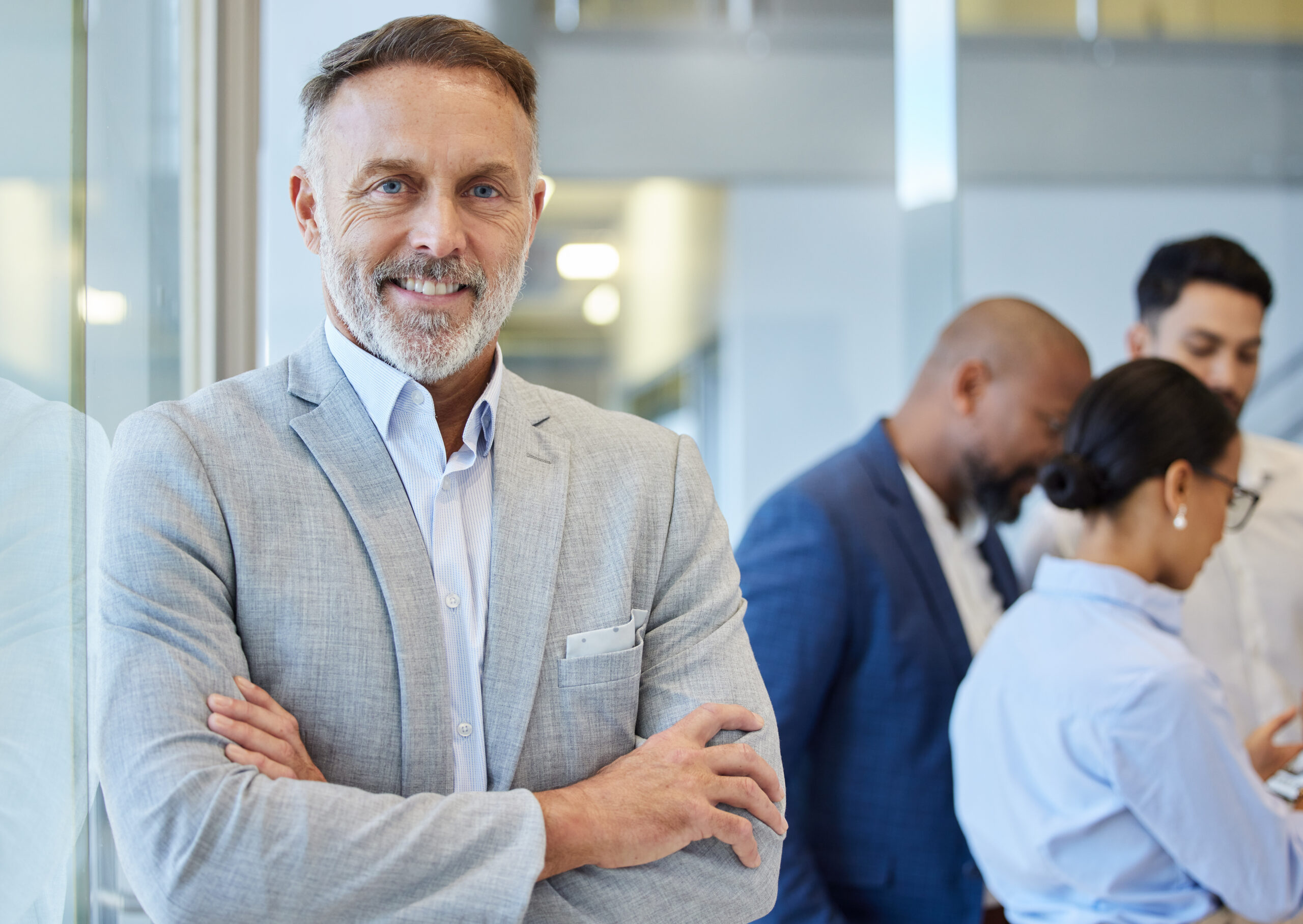 Portrait of a mature businessman standing in an office with his colleagues in the background.